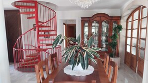 Un espace repas comprenant une table en bois, des chaises, un escalier en colimaçon rouge et un lustre.