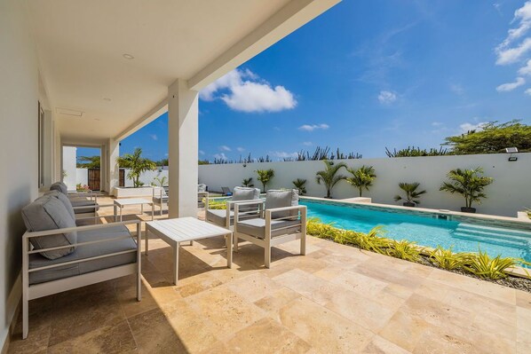 Un patio exterior moderno con piscina, zona de estar y vistas del paisaje circundante.