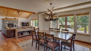 A spacious dining area with a large wooden table and chairs, a stone fireplace, and a modern chandelier.