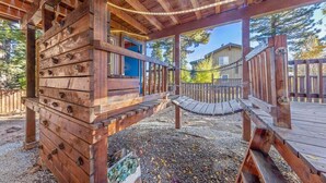 A wooden deck with a hammock, a wooden playhouse, and a chain-link fence.