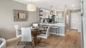 Una cocina moderna con una isla central, sillas blancas y una mesa de comedor.