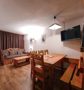 Uma sala de estar acolhedora com sofá, mesa de jantar de madeira, cadeiras, um banco, TV e luminária de teto.