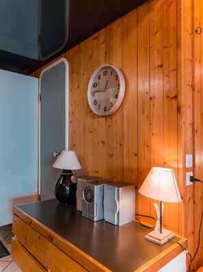 A wooden wall with a round wall clock, a wooden dresser with a lamp, and a washing machine.