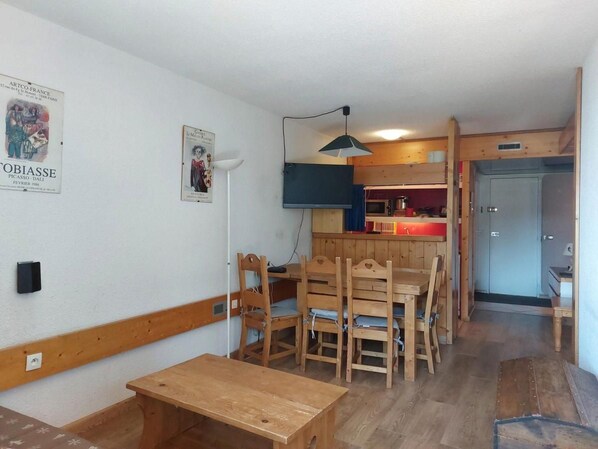 A room with a wooden dining table and chairs, a kitchenette with a red sink, and a ceiling lamp.