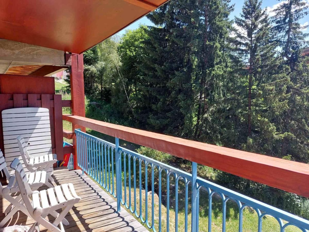 Una terraza de madera con barandal azul, con vistas a una zona boscosa.
