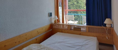 A bedroom with a bed, a window with a view of the outside, a wooden headboard, and a small table with a lamp.