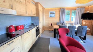 Et lille køkken med træskabe, et spiseområde med et bord og stole, og en rød stol.