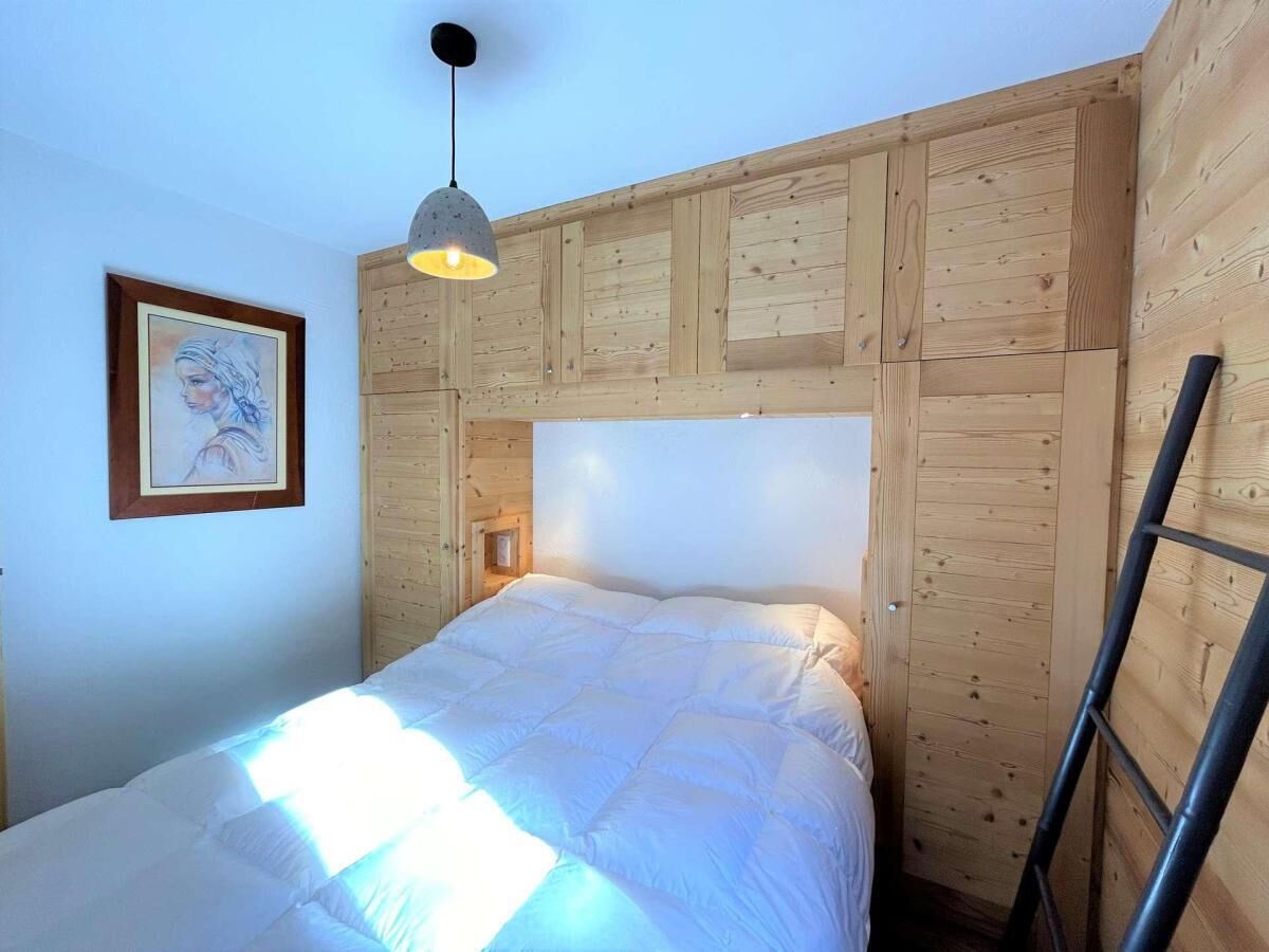 A bedroom with a wooden headboard, a bed with white bedding, a hanging light fixture, and a framed picture on the wall.