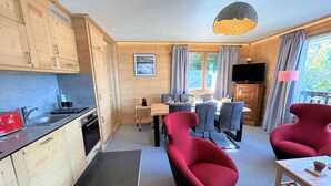 Et moderne køkken med træskabe, et spiseområde med grå stole og en rød lænestol.