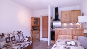 Un espace de vie compact comprenant un canapé, une table à manger avec un plateau, des meubles en bois et une petite cuisine.