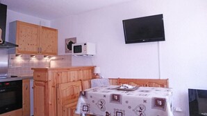 Une cuisine compacte dotée de meubles en bois, d’un four à micro-ondes et d’un téléviseur à écran plat fixé au mur.
