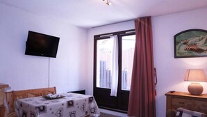 Une pièce comprenant une table, un téléviseur fixé au mur, une fenêtre avec des rideaux et une lampe sur une table de chevet.