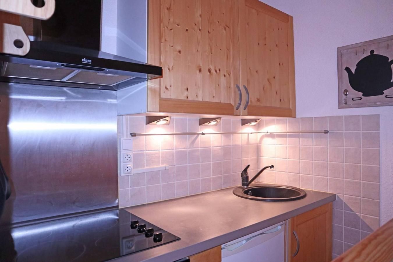 Une cuisine équipée d’une cuisinière en acier inoxydable, de meubles en bois, d’un pare-feu en carreaux et d’une bouilloire fixée au mur.