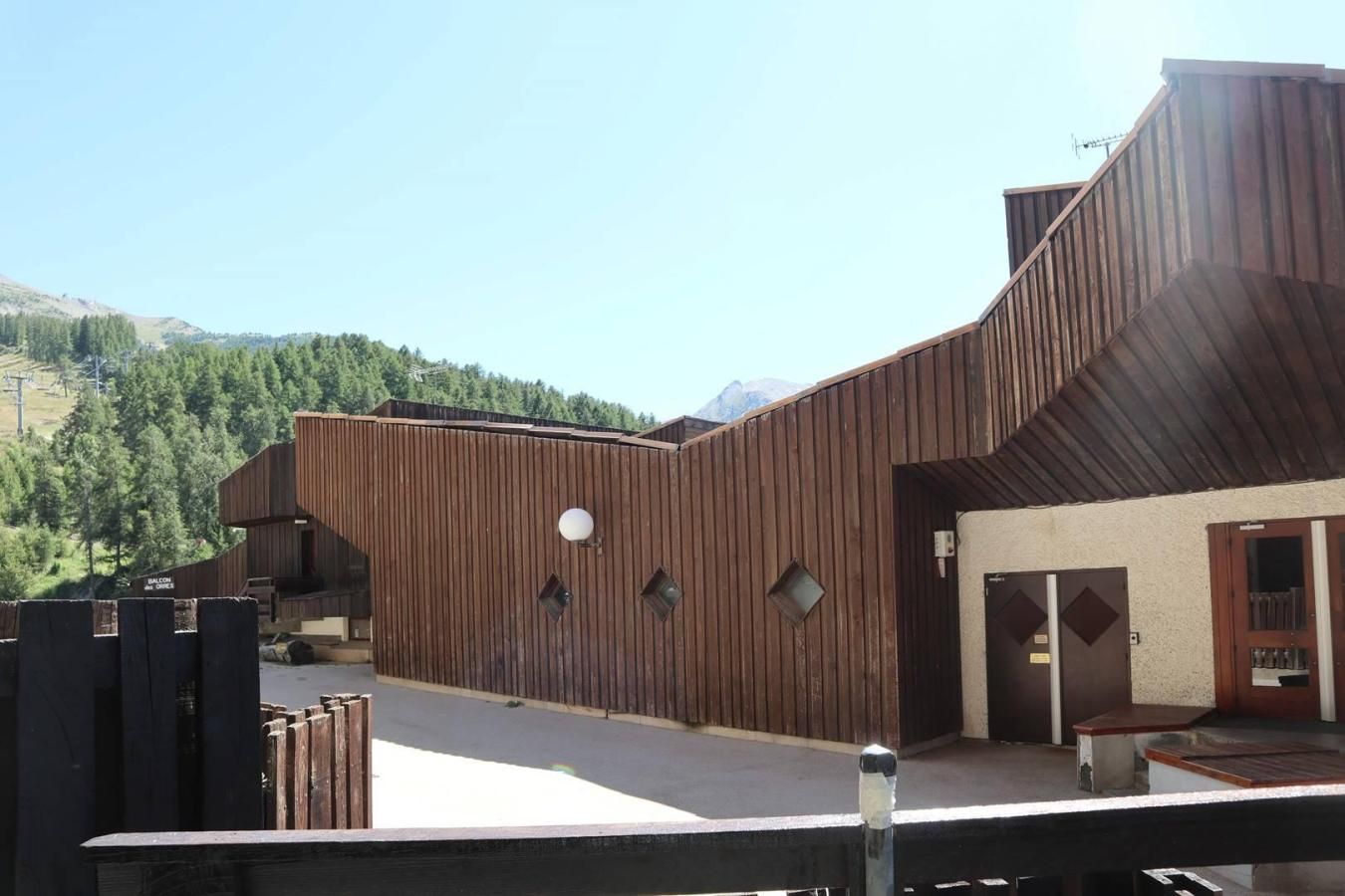 A modern building with a wooden exterior, a balcony, and a door with a window.