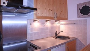 Une cuisine de taille réduite, dotée d’une cuisinière en acier inoxydable, d’un seul évier et d’armoires en bois.