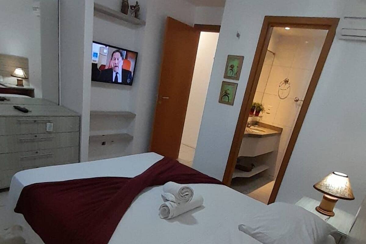 Una habitación de hotel con una cama, un televisor en la pared, un espejo y una lámpara.