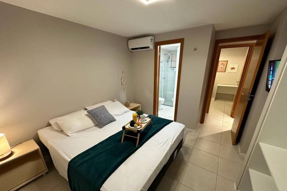Una cama bien hecha con una manta verde, una mesita de noche con una lámpara y una bandeja pequeña con cosas para el desayuno.