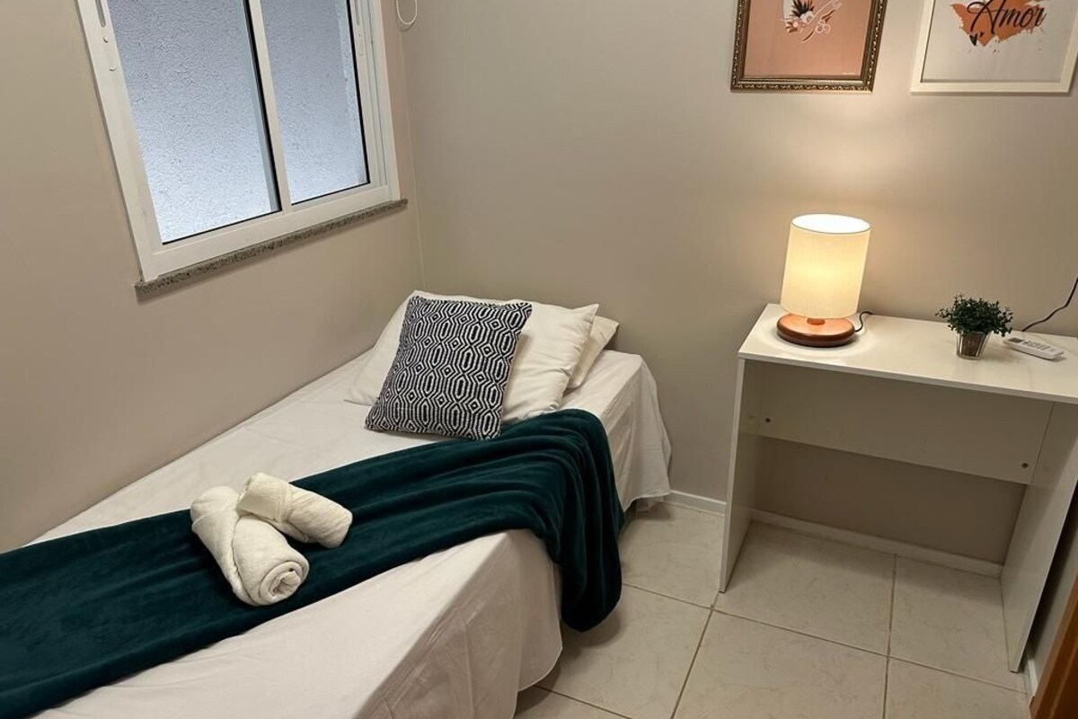 Une petite chambre à coucher, bien rangée, avec un lit, des oreillers, une lampe de chevet et un petit bureau avec une lampe.