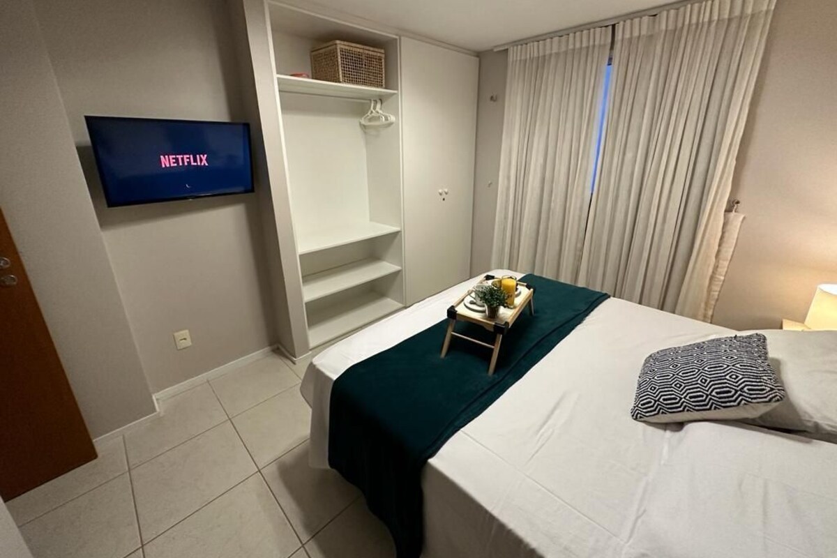 A hotel room with a bed, a TV displaying 'NETFLIX', a wardrobe, and a window with curtains.