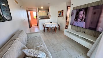 A living room with a sofa, TV, dining area, and kitchen in the background.