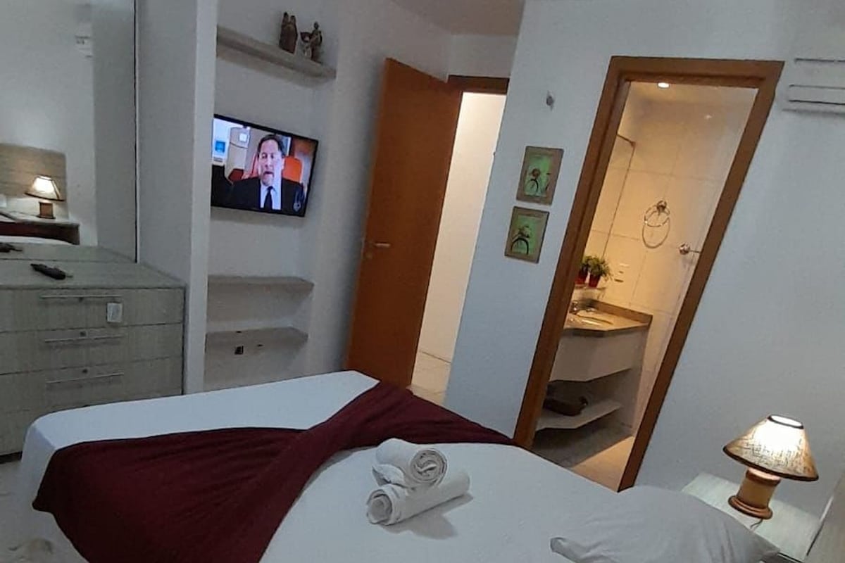 A hotel room with a bed, a TV on the wall, a mirror, and a lamp.