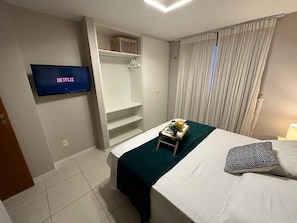 A hotel room with a bed, a TV displaying 'NETFLIX', a wardrobe, and a window with curtains. - Porto Beach Conforto e Lazer a 200m do B Park (Aquiraz)