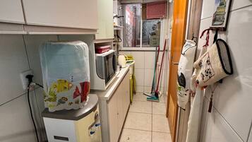 A narrow kitchen with white cabinets, a refrigerator, a microwave, and a window with a view.