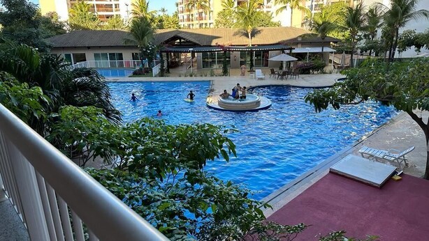 A swimming pool with a circular hot tub, surrounded by palm trees and a building with balconies. - Porto Beach Conforto e Lazer a 200m do B Park (Aquiraz)