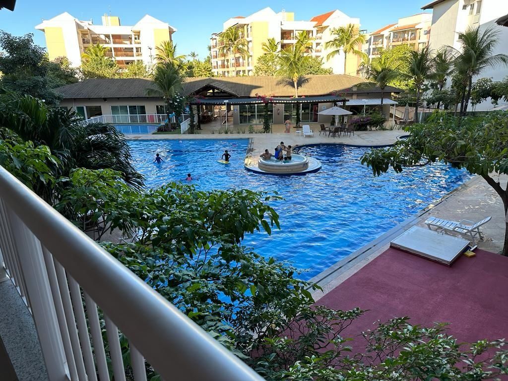 A swimming pool with a circular hot tub, surrounded by palm trees and a building with balconies.