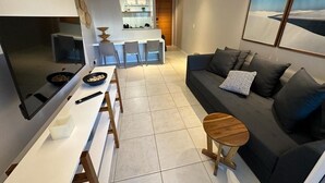 A modern living room with a sofa, a dining table, and a kitchen area in the background. - Porto Beach Conforto e Lazer a 200m do B Park (Aquiraz)