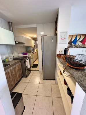 A kitchen with a stainless steel refrigerator, a microwave, and a sink. There is a tiled floor and a countertop with various items. - Porto Beach Conforto e Lazer a 200m do B Park (Aquiraz)