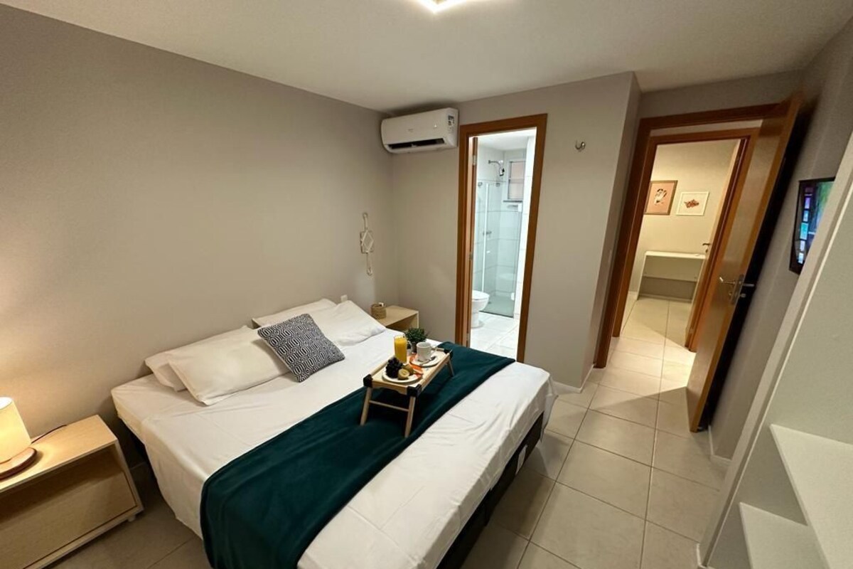 A neatly made bed with a green blanket, a bedside table with a lamp, and a small tray with breakfast items.