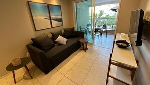A living room with a sofa, a small table, a TV, and a balcony with chairs. - Porto Beach Conforto e Lazer a 200m do B Park (Aquiraz)
