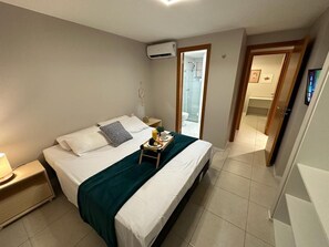 A neatly made bed with a green blanket, a bedside table with a lamp, and a small tray with breakfast items. - Porto Beach Conforto e Lazer a 200m do B Park (Aquiraz)