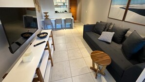 A modern living room with a sofa, a dining table, and a kitchen area in the background. - Porto Beach Conforto e Lazer a 200m do B Park (Aquiraz)