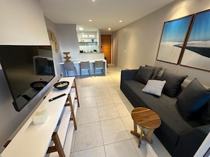 A modern living room with a sofa, a dining table, and a kitchen area in the background. - Porto Beach Conforto e Lazer a 200m do B Park (Aquiraz)