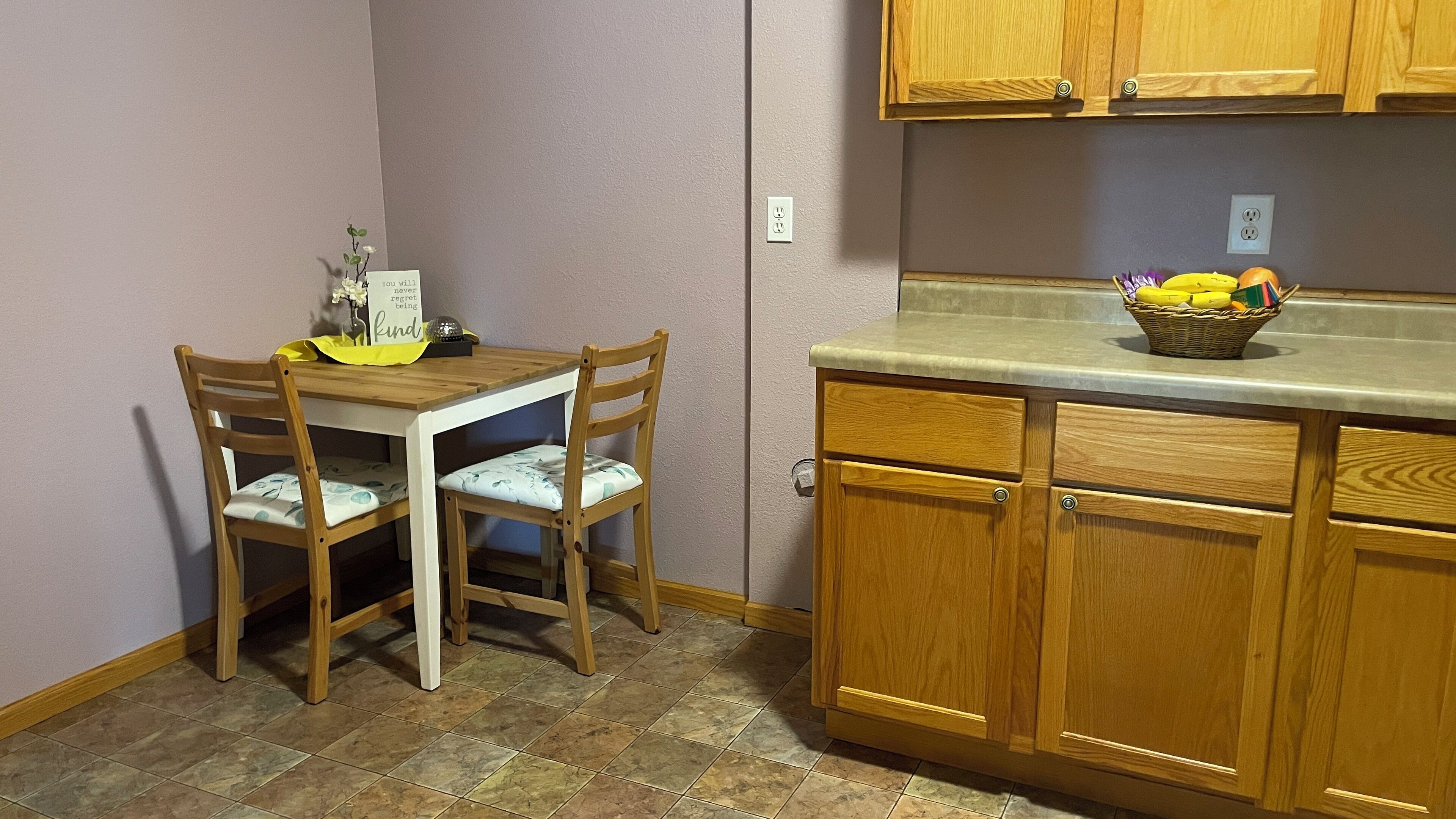 Une petite cuisine avec des meubles de rangement en bois, un plan de travail et une table à manger avec des chaises.
