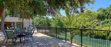 An outdoor deck with a table and chairs, a railing, and a view of a river.