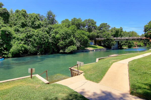 A river with a wooden bridge, a concrete walkway, and lush greenery.