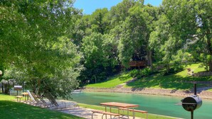 Ein Picknickbereich mit Tisch und Bänken an einem Fluss, umgeben von Bäumen.