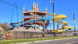 Ein Wasserpark mit einem schlösserartigen Bauwerk, mehreren Wasserrutschen und einem eingezäunten Bereich mit einem Mülleimer.