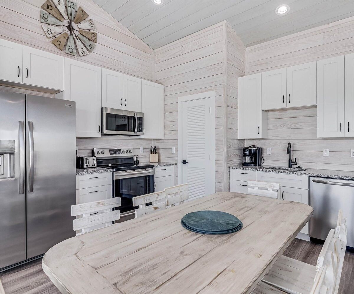 Una cocina moderna con armarios blancos, electrodomésticos de acero inoxidable y una mesa de comedor de madera.