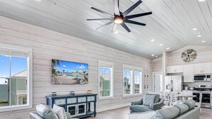 A spacious living area with a large window, a ceiling fan, and a dining area with a kitchen in the background. - Sunshine And Flip Flops Sp114 4 Bedroom Home by RedAwning (Fulton)