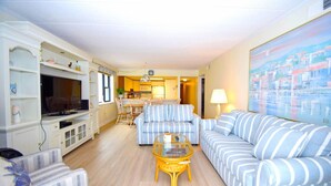 A living room with striped sofas, a glass coffee table, and a TV on a cabinet. - Amber Waves 300 3 Bedroom Condo by RedAwning (Ocean City)