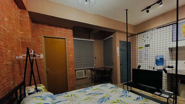 A room with a bed, a desk, and a TV. There is a brick wall and a door. - 83 F. Bautista St (Quezon City)