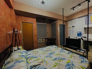 A room with a bed, a desk, and a TV. There is a brick wall and a door. - 83 F. Bautista St (Quezon City)