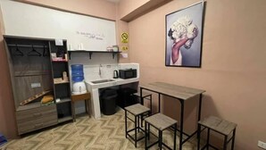 A compact kitchenette with a sink, microwave, and storage shelves. There is a small table with two stools and a large water dispenser. - 83 F. Bautista St (Quezon City)