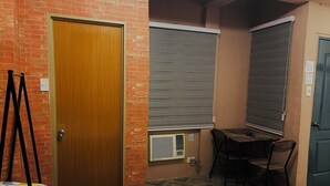 A room with a wooden door, a brick wall, a table with chairs, and a patterned rug. - 83 F. Bautista St (Quezon City)