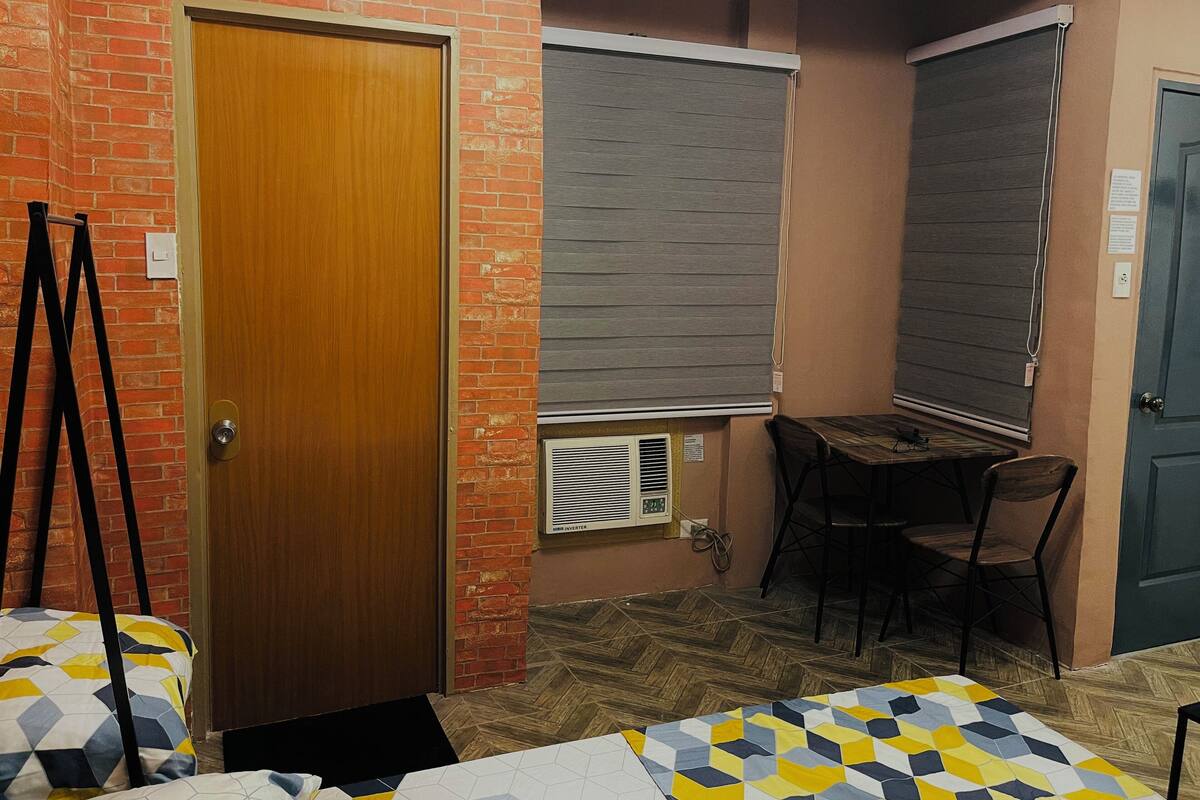 A room with a wooden door, a brick wall, a table with chairs, and a patterned rug.