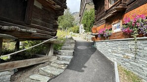 A narrow cobblestone path flanked by wooden buildings with stone walls and flower boxes.